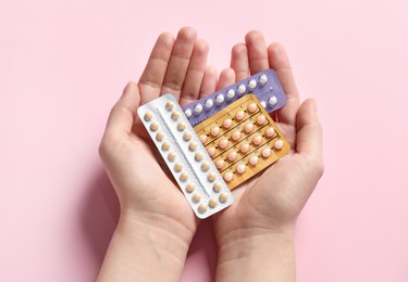 Woman holding blisters of contraceptive pills on pink background, closeup