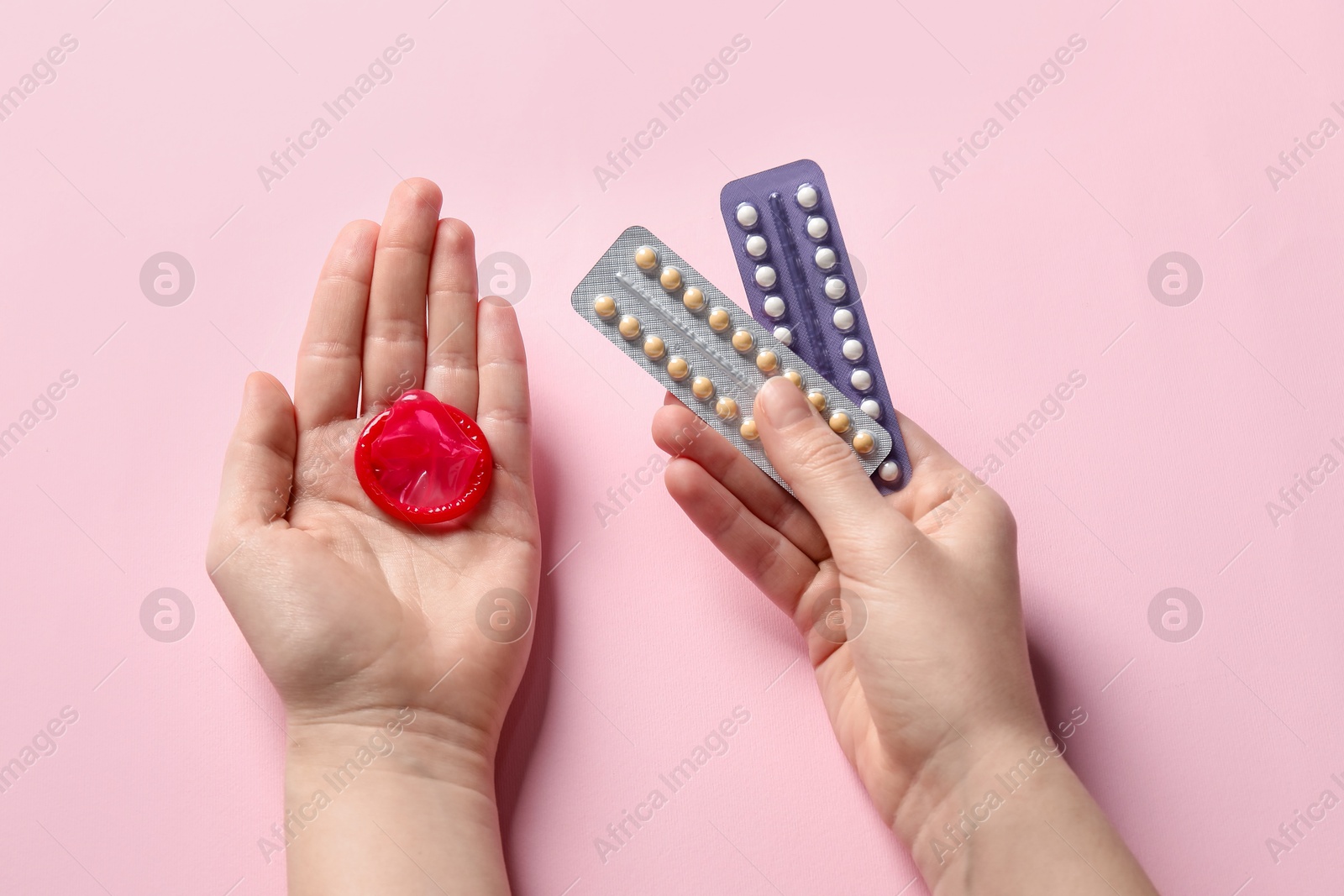 Photo of Woman holding blisters of contraceptive pills and condom on pink background, closeup