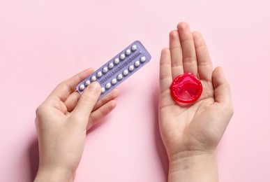 Photo of Woman holding blister of contraceptive pills and condom on pink background, closeup