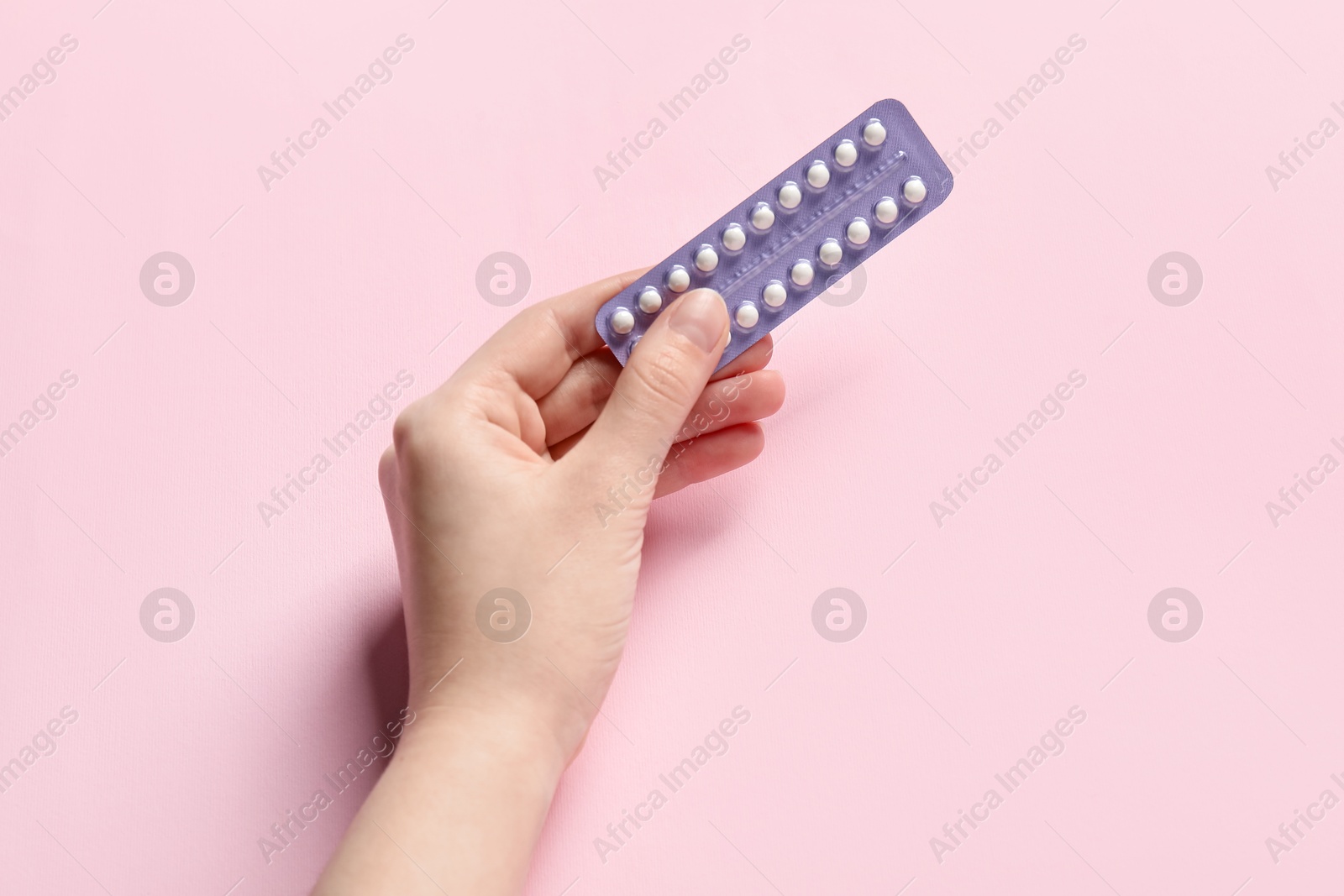 Photo of Woman holding blister of contraceptive pills on pink background, closeup