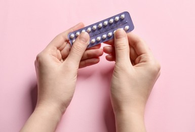 Photo of Woman holding blister of contraceptive pills on pink background, closeup