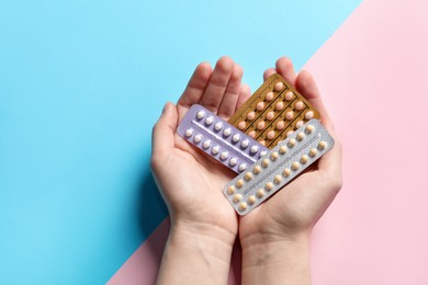 Woman holding blisters of contraceptive pills on color background, closeup