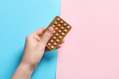 Photo of Woman holding blister of contraceptive pills on color background, closeup. Space for text