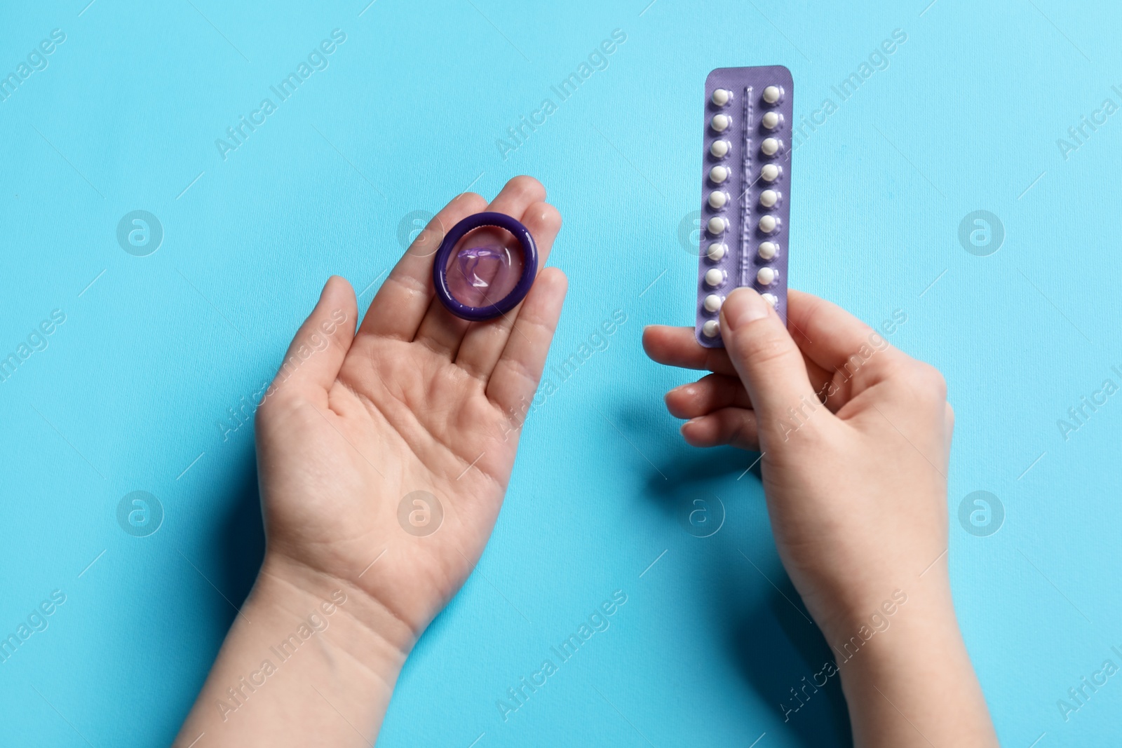 Photo of Woman holding blister of contraceptive pills and condom on light blue background, closeup