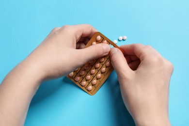 Woman taking contraceptive pill out from blister on light blue background, closeup