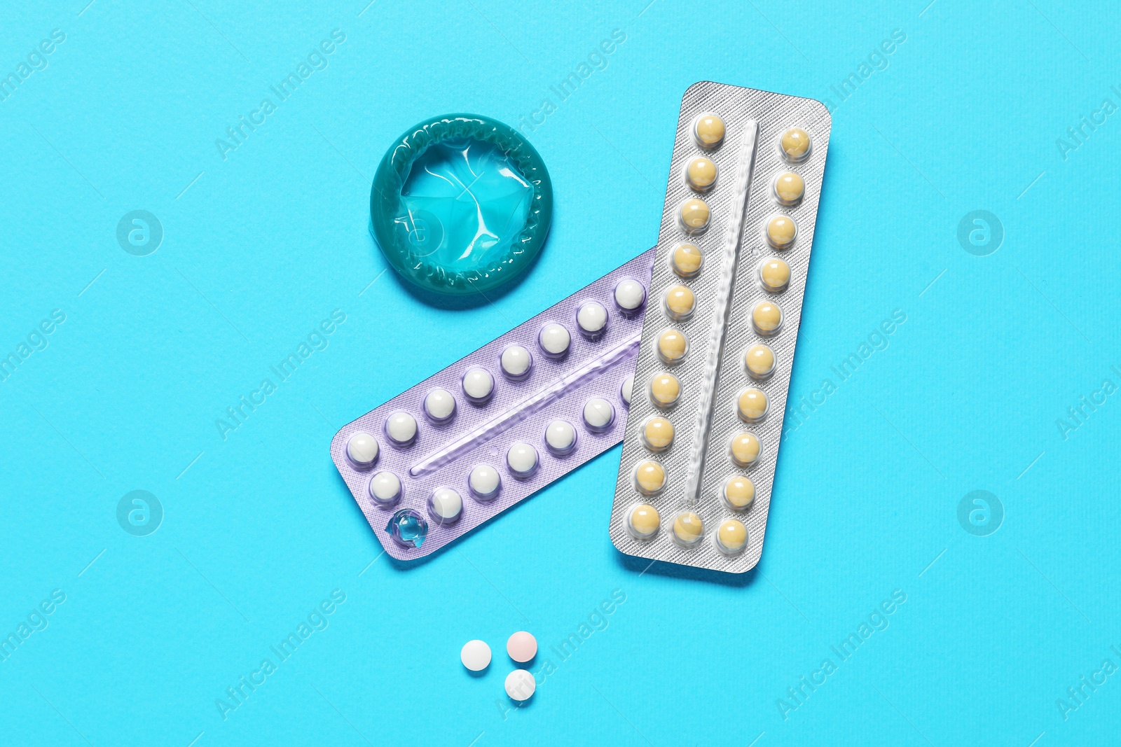 Photo of Contraceptive pills and condom on light blue background, flat lay