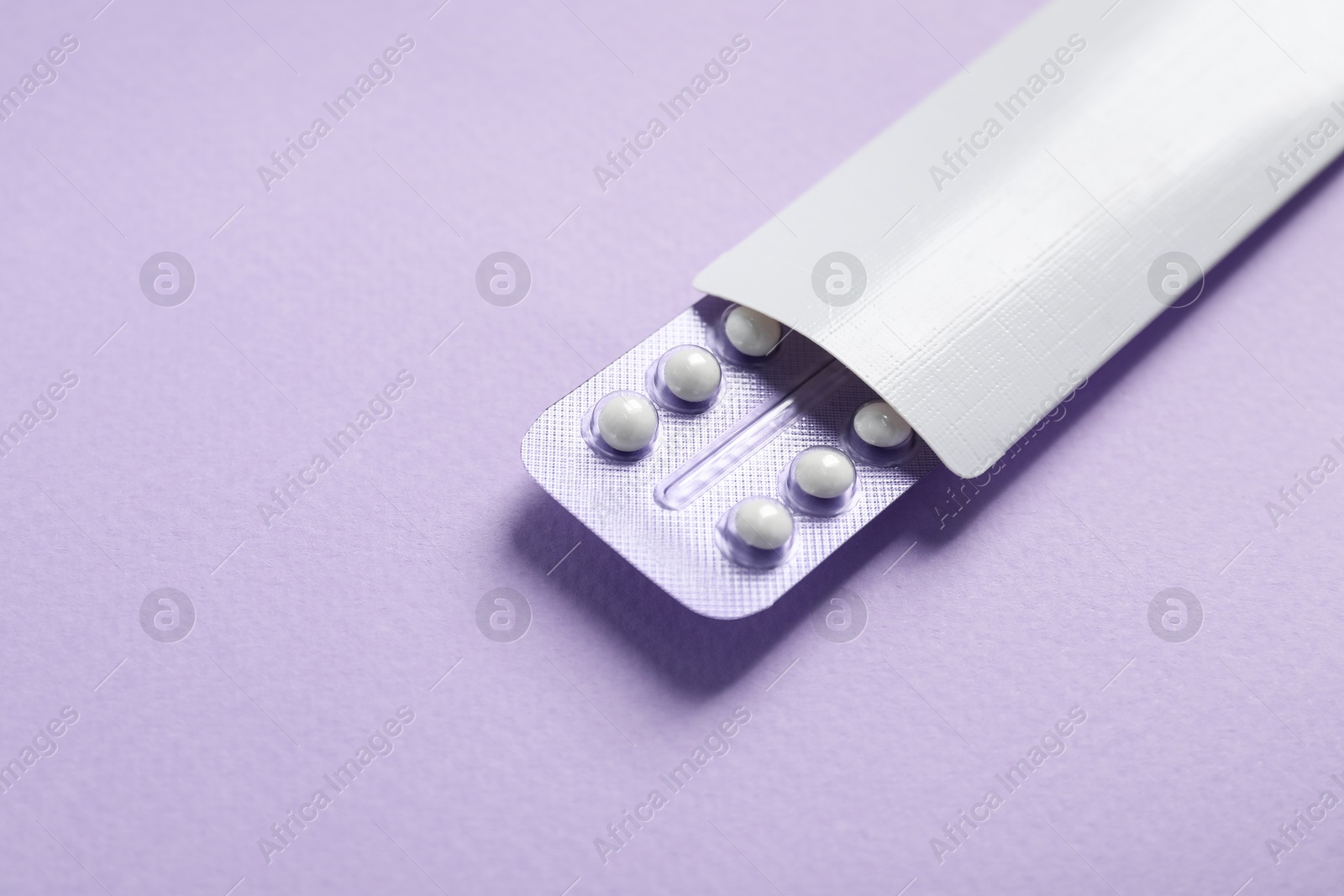 Photo of Blister of contraceptive pills in package on lilac background, closeup. Space for text