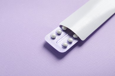 Blister of contraceptive pills in package on lilac background, closeup. Space for text