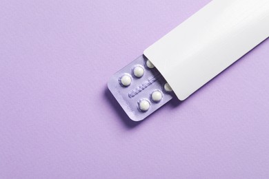 Photo of Blister of contraceptive pills in package on lilac background, top view. Space for text