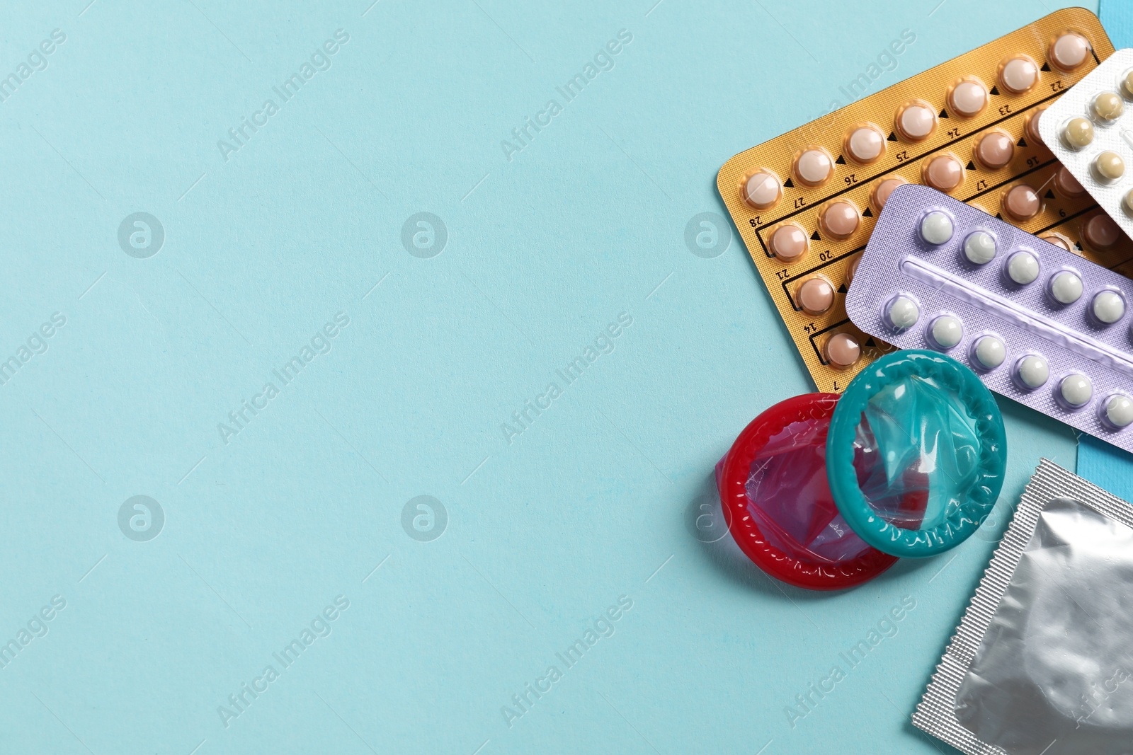 Photo of Blisters of contraceptive pills and condoms on light blue background, flat lay. Space for text