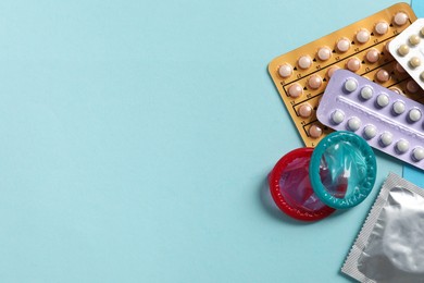 Blisters of contraceptive pills and condoms on light blue background, flat lay. Space for text