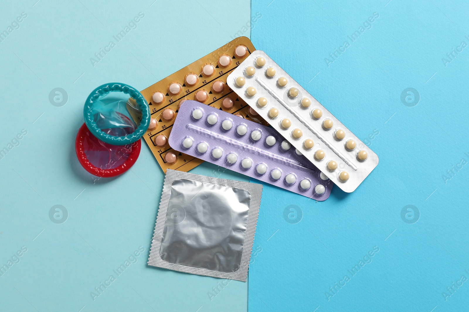 Photo of Blisters of contraceptive pills and condoms on light blue background, flat lay