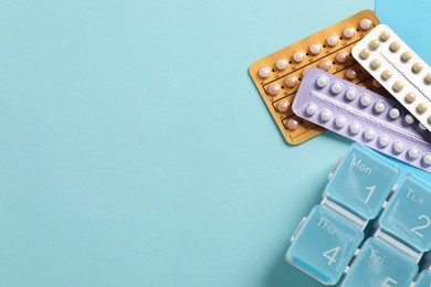 Photo of Blisters of contraceptive pills and organizer on light blue background, flat lay. Space for text