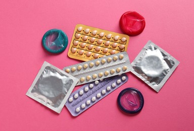 Blisters of contraceptive pills and condoms on pink background, flat lay