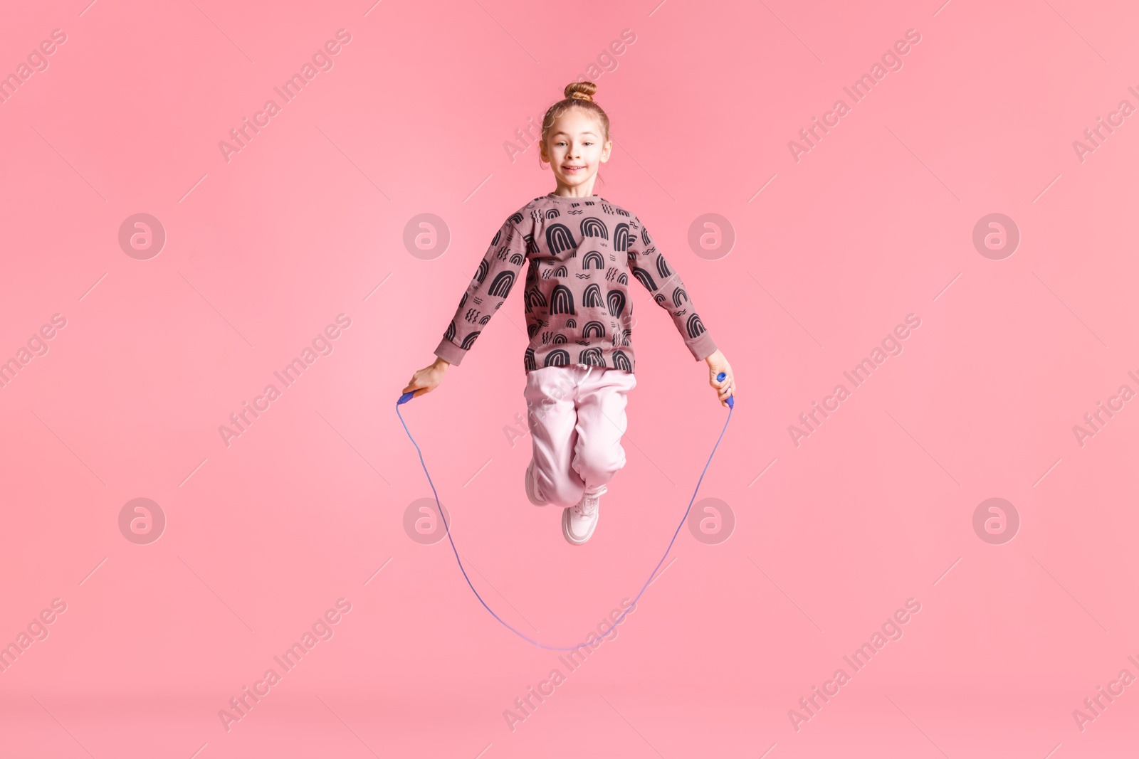 Photo of Cute little girl with jump rope on light pink background