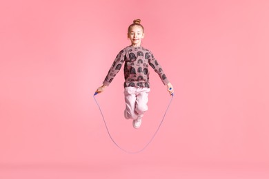 Photo of Cute little girl with jump rope on light pink background