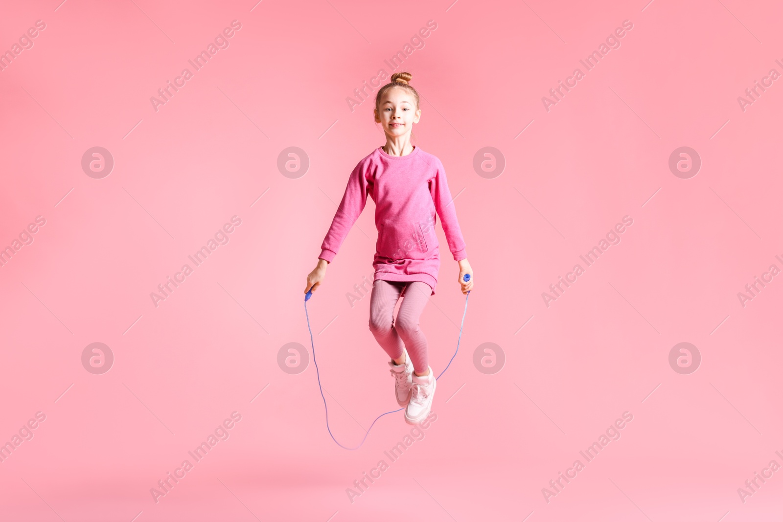 Photo of Cute little girl with jump rope on light pink background