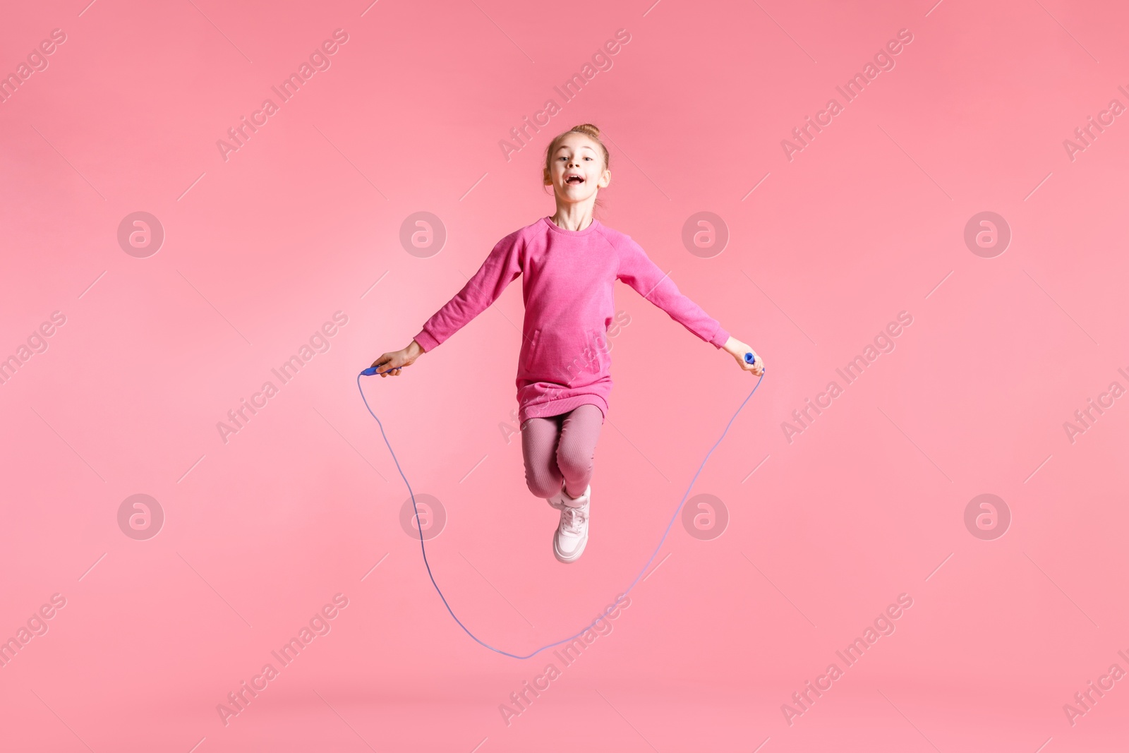 Photo of Cute little girl with jump rope on light pink background