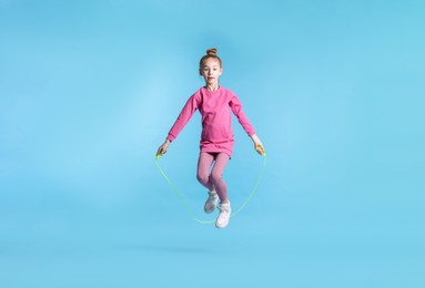 Photo of Cute little girl with jump rope on light blue background