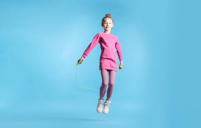 Photo of Cute little girl with jump rope on light blue background