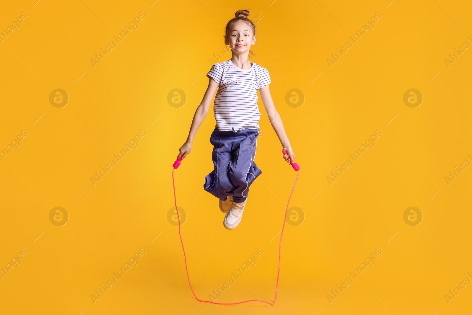 Photo of Cute little girl with jump rope on orange background