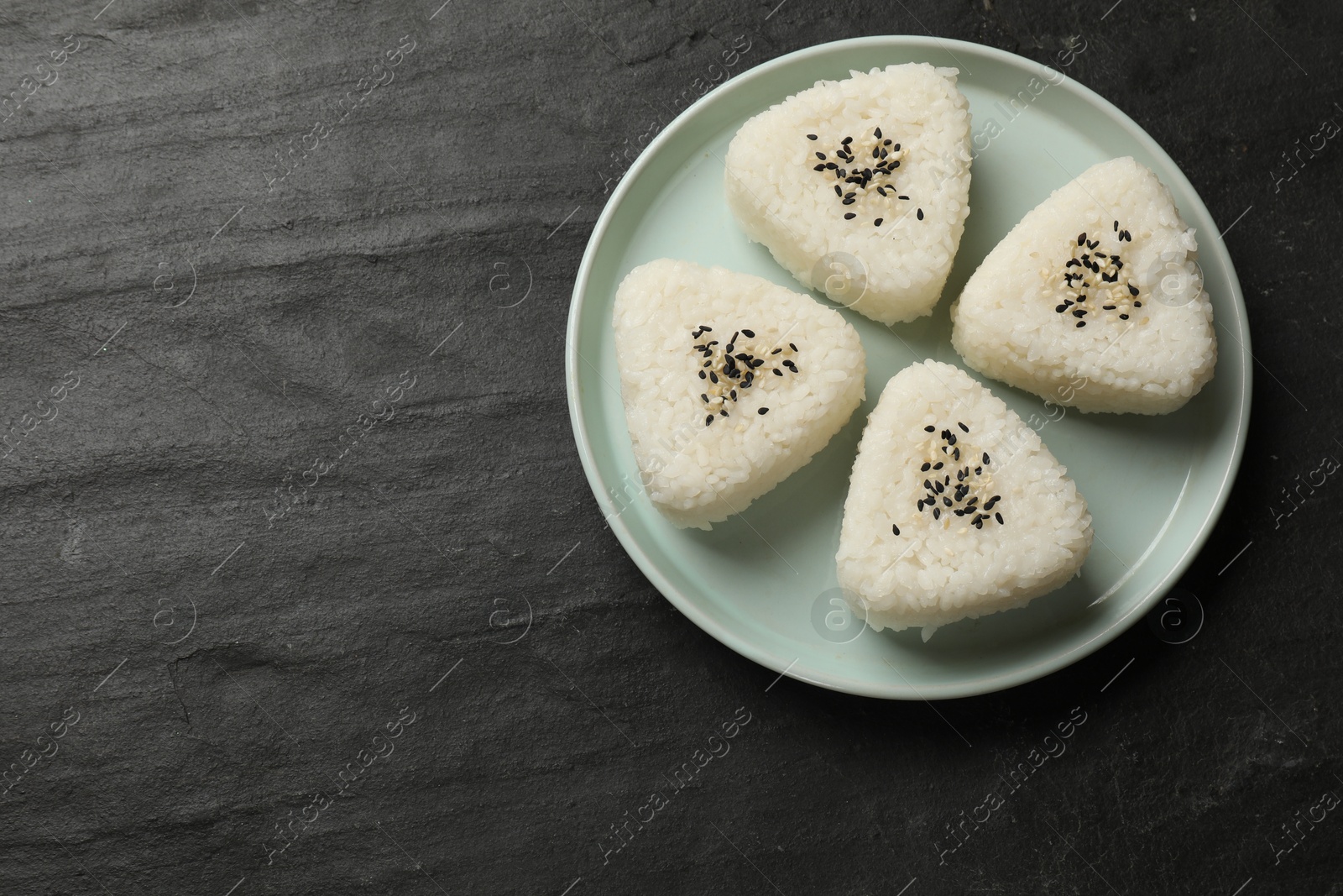 Photo of Tasty onigiri (Japanese rice balls) on black table, top view. Space for text