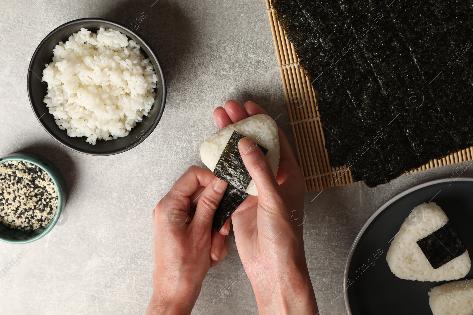 Photo of Woman making tasty onigiri (Japanese rice balls) at light table, top view