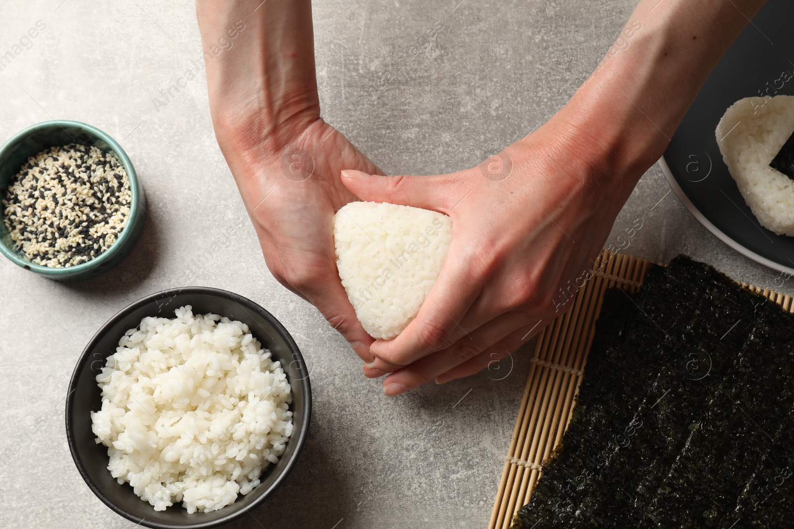 Photo of Woman making tasty onigiri (Japanese rice balls) at light table, top view