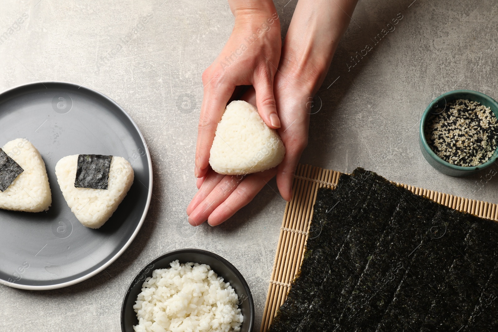 Photo of Woman making tasty onigiri (Japanese rice balls) at light table, top view