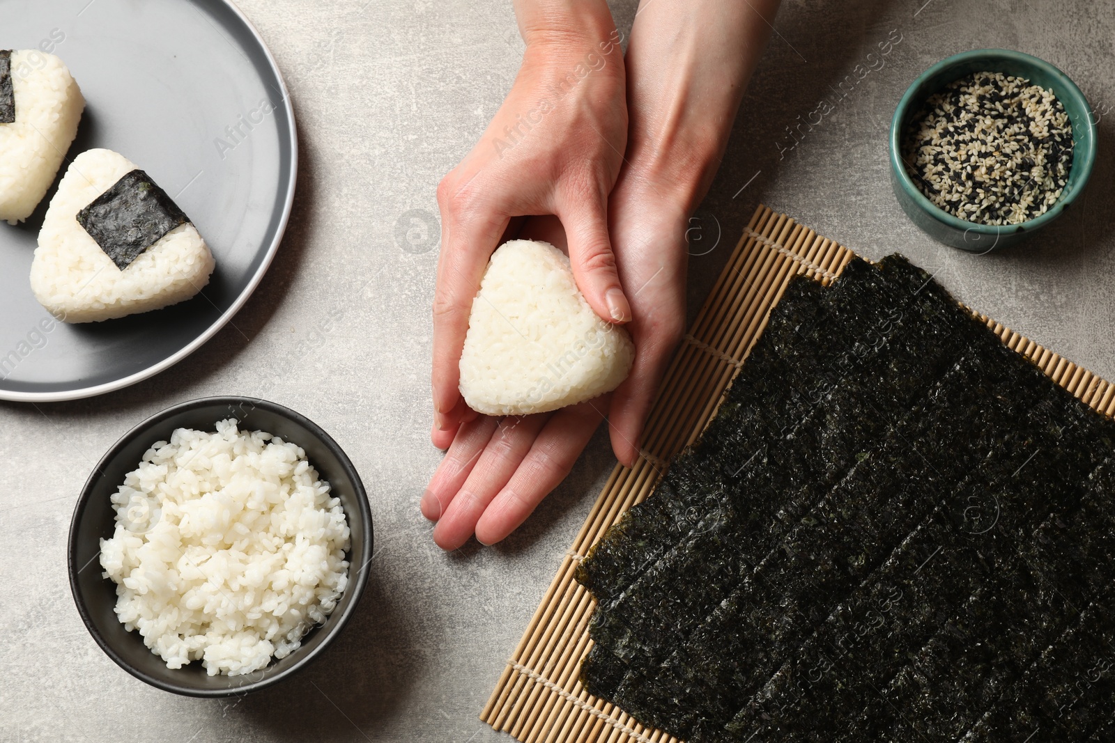 Photo of Woman making tasty onigiri (Japanese rice balls) at light table, top view