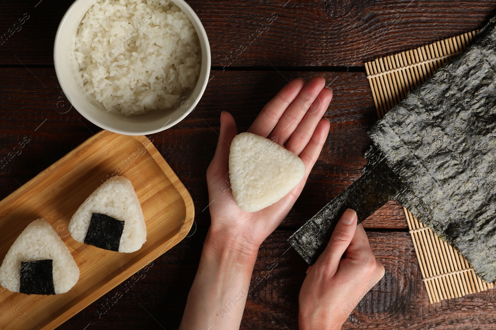 Photo of Woman making tasty onigiri (Japanese rice balls) at wooden table, top view