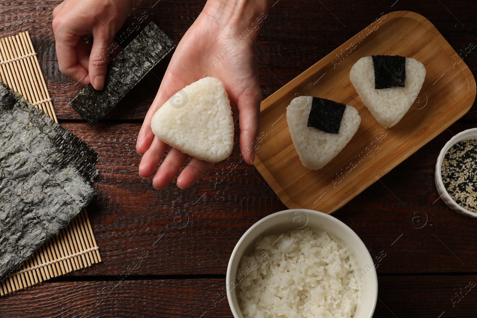 Photo of Woman making tasty onigiri (Japanese rice balls) at wooden table, top view