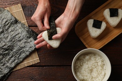 Photo of Woman making tasty onigiri (Japanese rice balls) at wooden table, top view