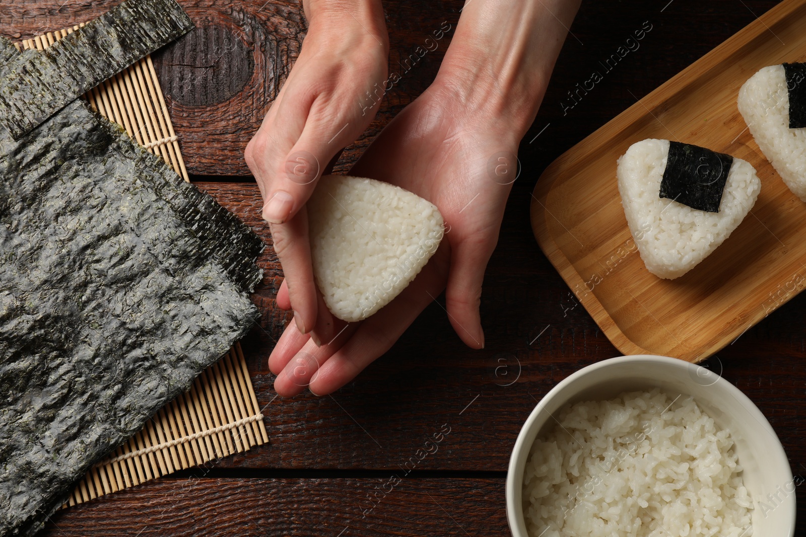 Photo of Woman making tasty onigiri (Japanese rice balls) at wooden table, top view