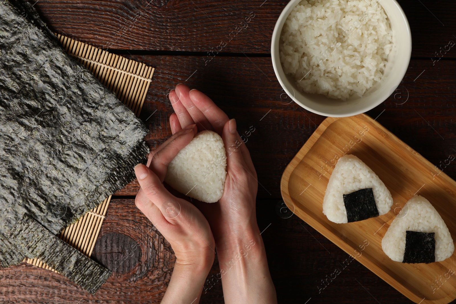 Photo of Woman making tasty onigiri (Japanese rice balls) at wooden table, top view