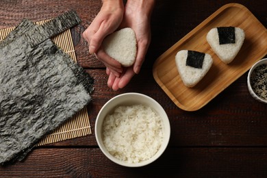 Photo of Woman making tasty onigiri (Japanese rice balls) at wooden table, top view