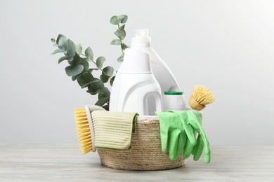 Photo of Eco-friendly cleaning products, supplies and eucalyptus branches in wicker basket on wooden table