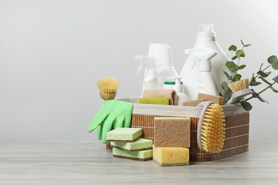 Photo of Eco-friendly cleaning products, supplies and eucalyptus branches in wicker basket on wooden table, space for text