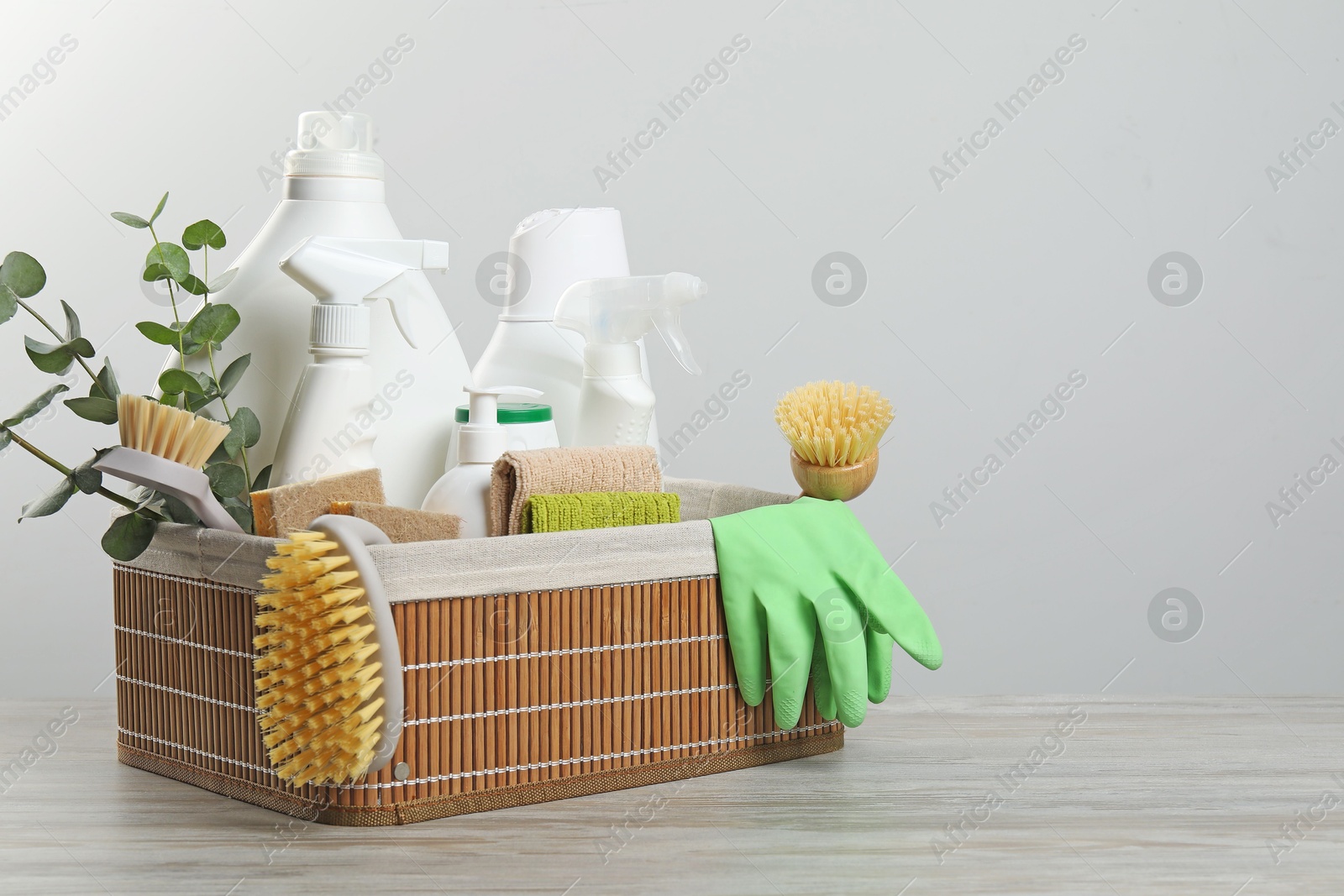 Photo of Eco-friendly cleaning products, supplies and eucalyptus branches in wicker basket on wooden table, space for text