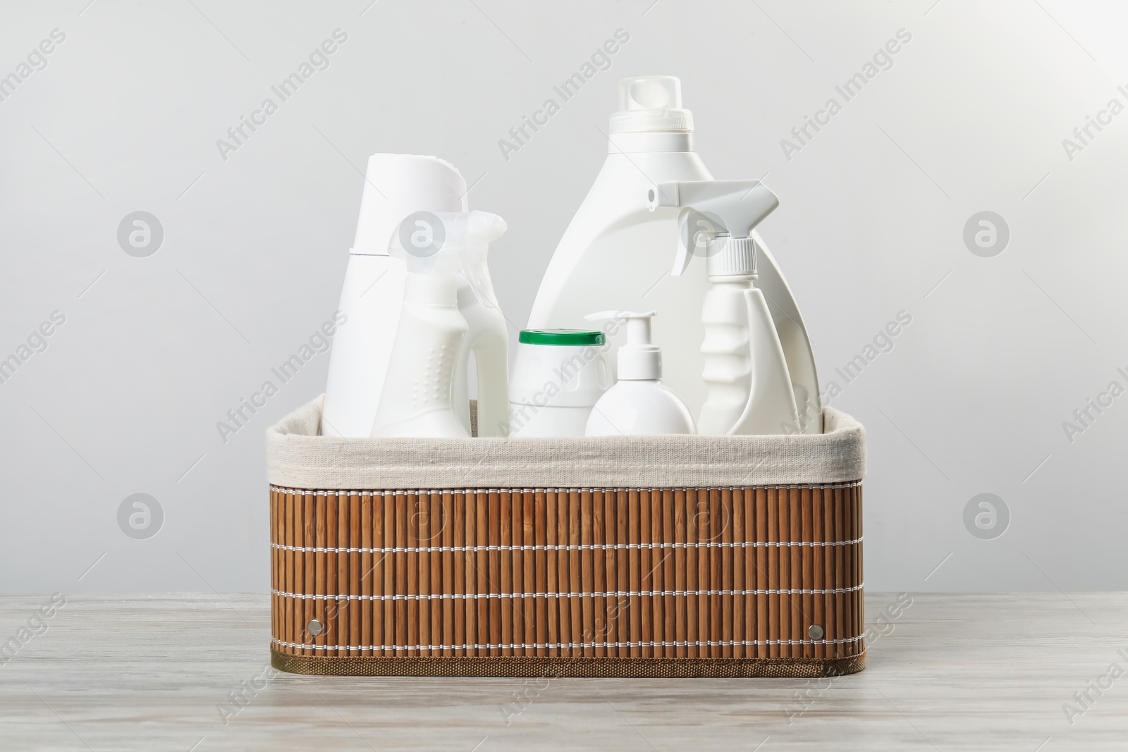 Photo of Different cleaning products in wicker basket on wooden table