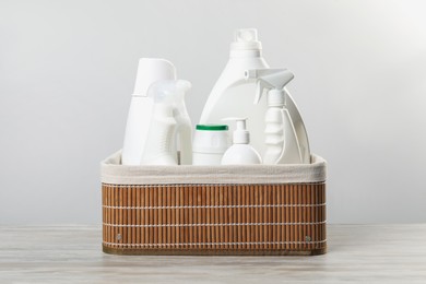 Photo of Different cleaning products in wicker basket on wooden table