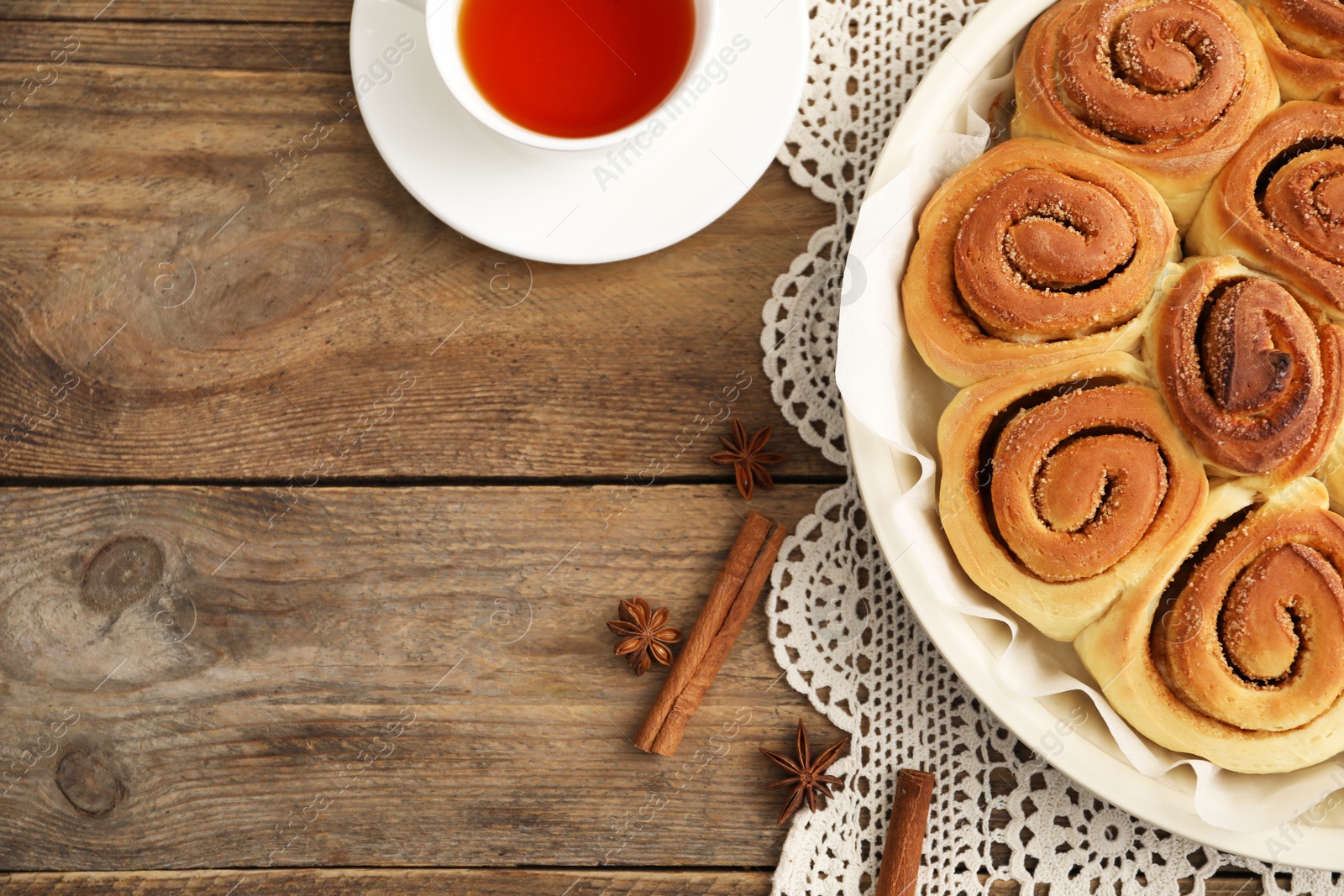 Photo of Freshly baked cinnamon rolls, tea and spices on wooden table, flat lay. Space for text