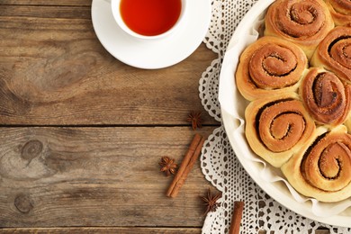 Photo of Freshly baked cinnamon rolls, tea and spices on wooden table, flat lay. Space for text