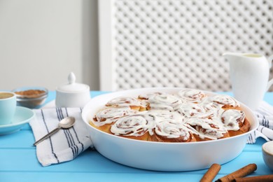 Delicious frosted cinnamon rolls in baking dish on light blue wooden table indoors, closeup