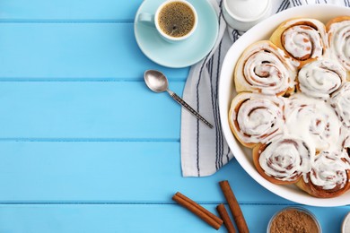 Delicious frosted cinnamon rolls in baking dish, coffee and spices on light blue wooden table, flat lay. Space for text