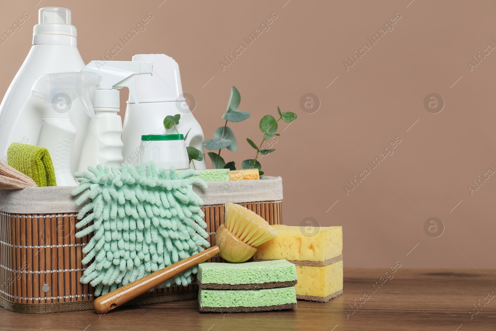 Photo of Eco-friendly cleaning products, supplies and eucalyptus branches in basket on wooden table, space for text