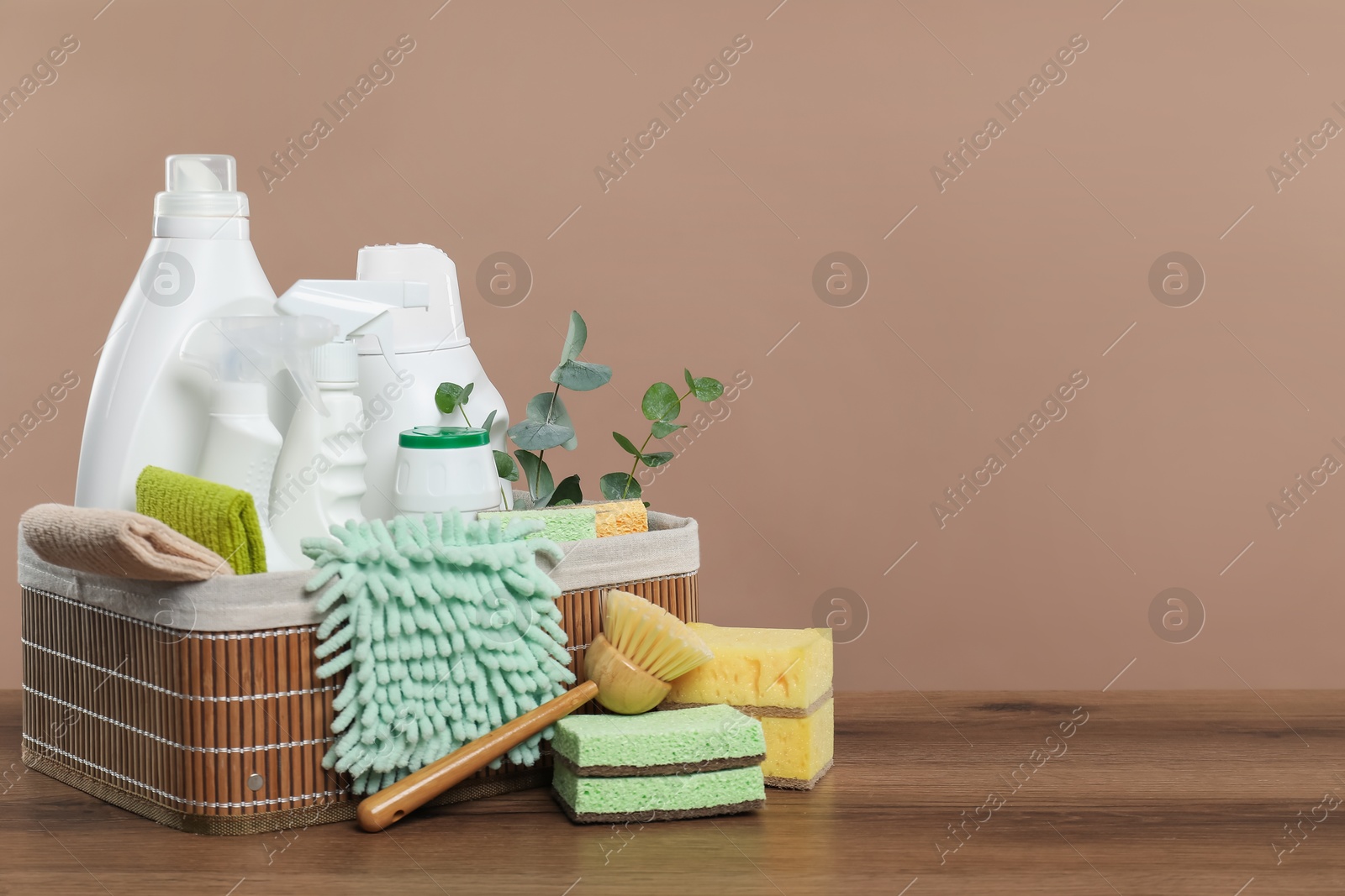 Photo of Eco-friendly cleaning products, supplies and eucalyptus branches in basket on wooden table, space for text