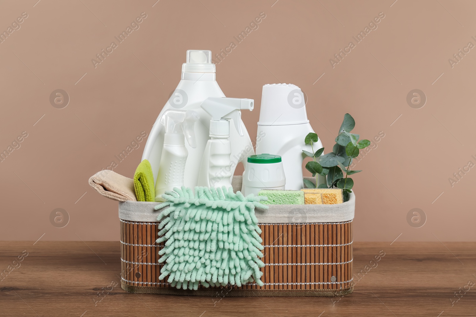 Photo of Eco-friendly cleaning products, supplies and eucalyptus branches in wicker basket on wooden table against beige background