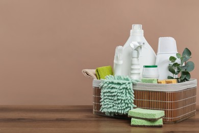 Photo of Eco-friendly cleaning products, supplies and eucalyptus branches in wicker basket on wooden table, space for text