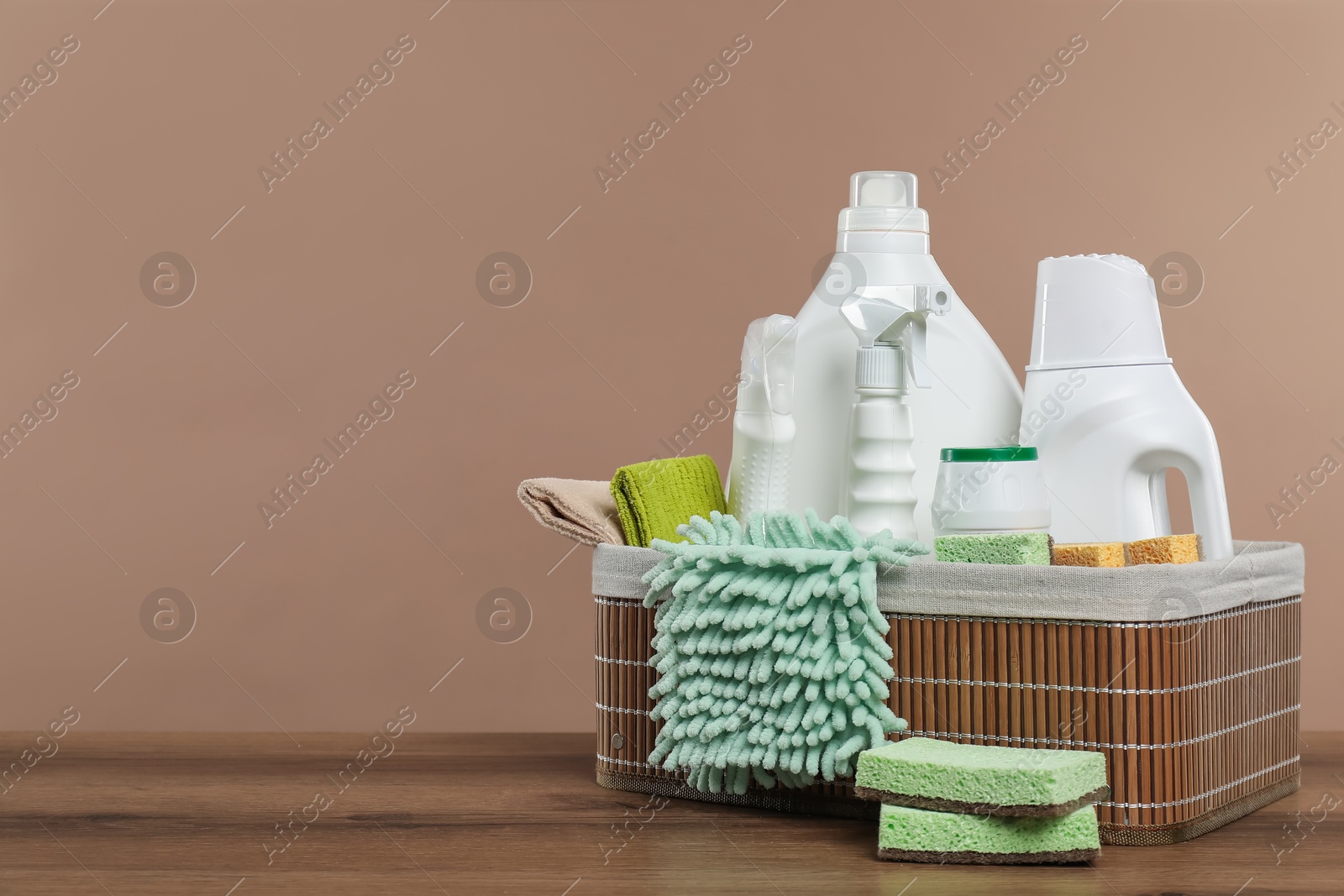 Photo of Eco-friendly cleaning products and supplies in wicker basket on wooden table against beige background, space for text